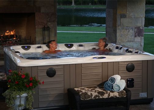 A couple talking in a hot tub with fireplace and lake in the background.